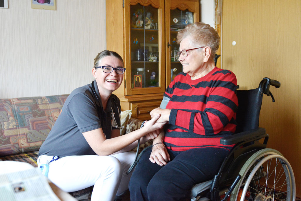 Pflegerin hält die Hand einer im Rollstuhl sitzenden Frau.