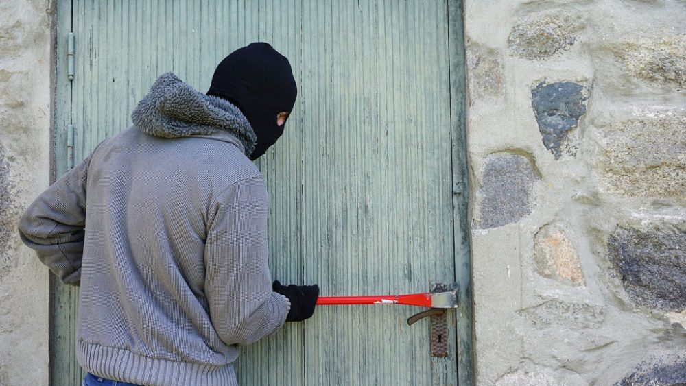 Einbrecher mit Kaputze und Brechstange an einer Tür