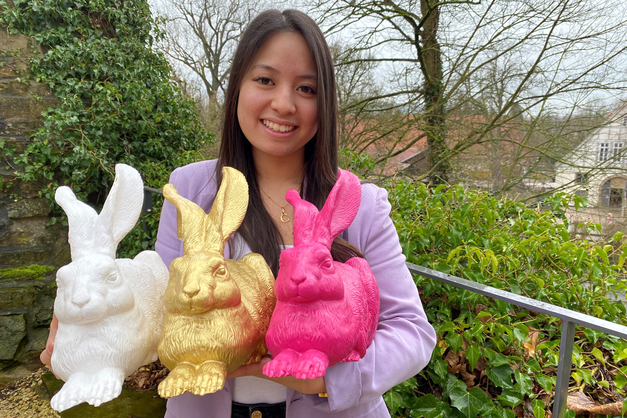 junge Frau hält drei verschiedenfarbige Hasen aus Plastik.